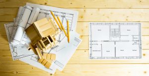 Many drawings for building, pencils and small house on wooden background.